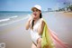 A woman in a white bathing suit and hat on the beach.