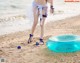 A woman in a bikini standing on a beach next to an inflatable pool.