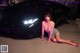 A woman sitting on the ground next to a black car.