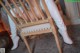 A woman sitting on a wooden chair wearing white pants and boots.