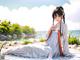 A woman in a white dress sitting on a blanket by the water.