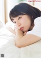 A woman laying on top of a bed with her hand on her chin.