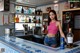 A woman standing behind a bar holding a bottle of alcohol.