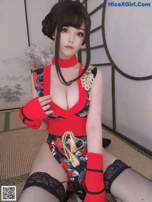 A woman in a red and black dress sitting on a bed.