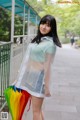 A woman in a clear raincoat holding a bunch of umbrellas.