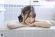 A woman laying in a bathtub with her hands on her head.